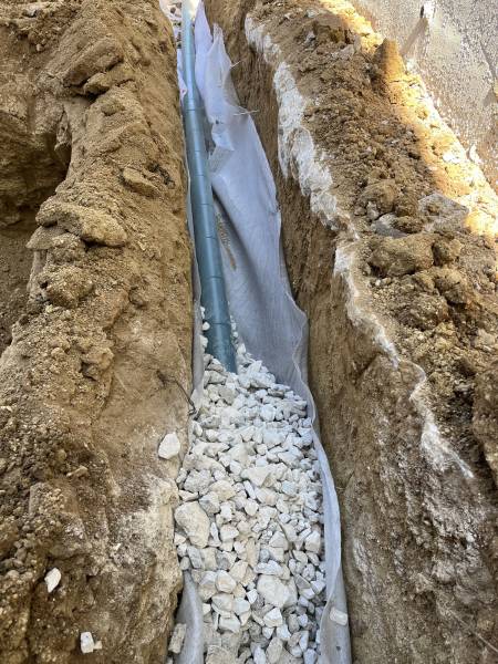 Pose d’un drain rigide sur lit de gravier, enrobé de géotextile filtrant contre la fondation